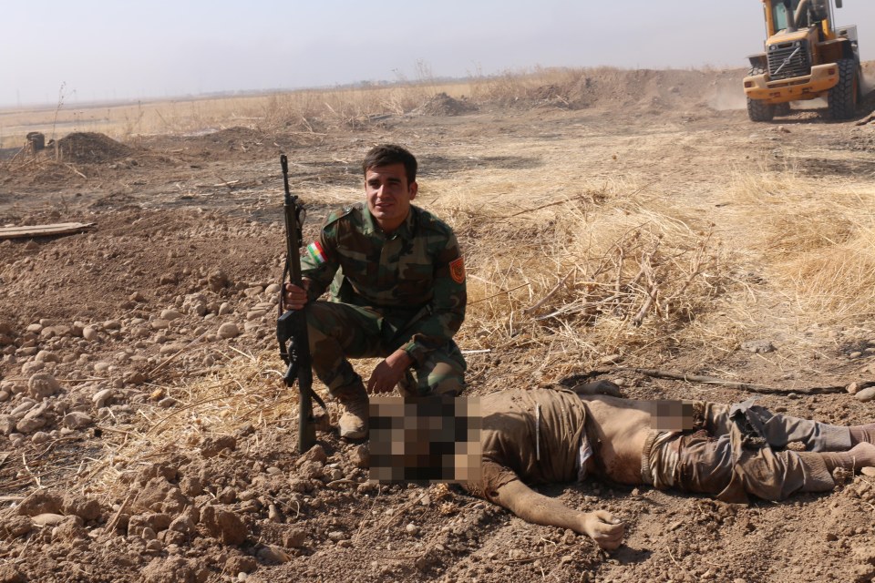 A Kurdish fighter poses next to the mangled corpse of an ISIS fighter