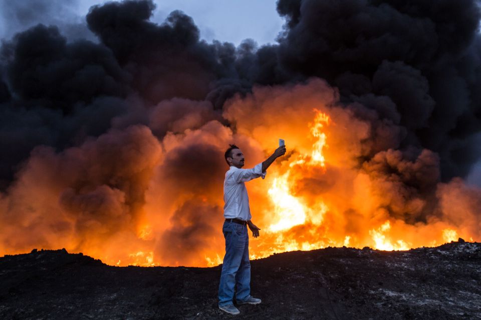  A man poses to take a selfie in front of the billowing oil well fire