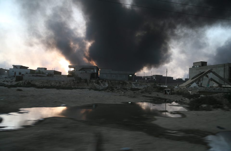  Oil slicks are seen spread across the ground as smoke rises in the background