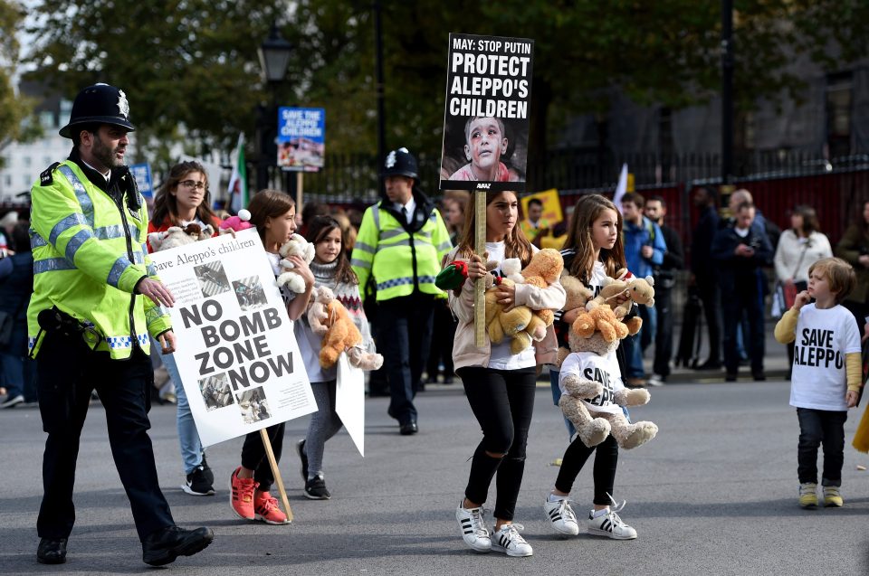  Protesters alongside police officers hold sings encouraging Theresa May to help protect Aleppo's children