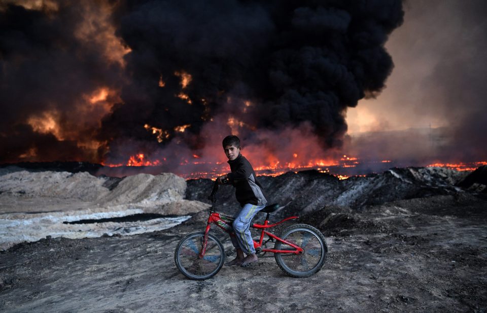  A boy pauses on his bike as he passes an oil field that was set on fire by retreating ISIS fighters