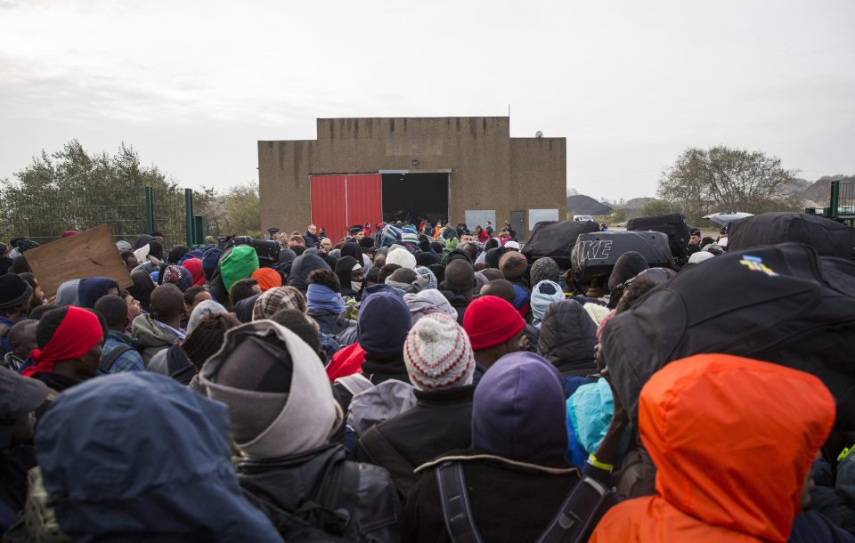 Today migrants are queuing at a reception point outside the Jungle migrant camp before boarding buses to refugee centres around France