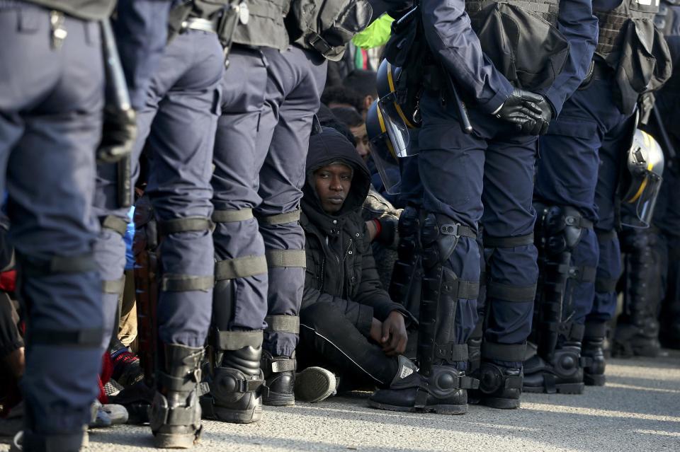 French police stand near as migrants wait in front of a processing centre to be registered on the second day of their evacuation and transfer to reception centers during the dismantlement of the "Jungle" in Calais