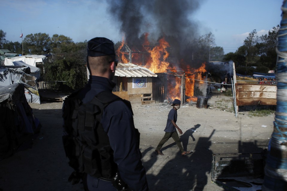 A French cop watches a ramshackle structure burn