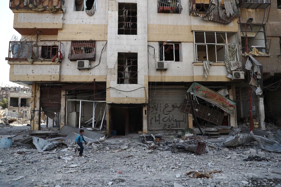  A child wanders past a damaged building in the town of Douma