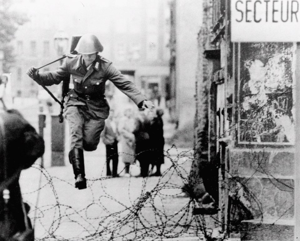 Defecting East German soldier Hans Conrad Schumann leaps over a barbed wire barricade at the Bernauer Street sector into West Berlin