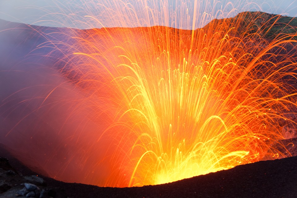 An explosion of Yasur volcano sends a shower of glowing lava bombs into the air