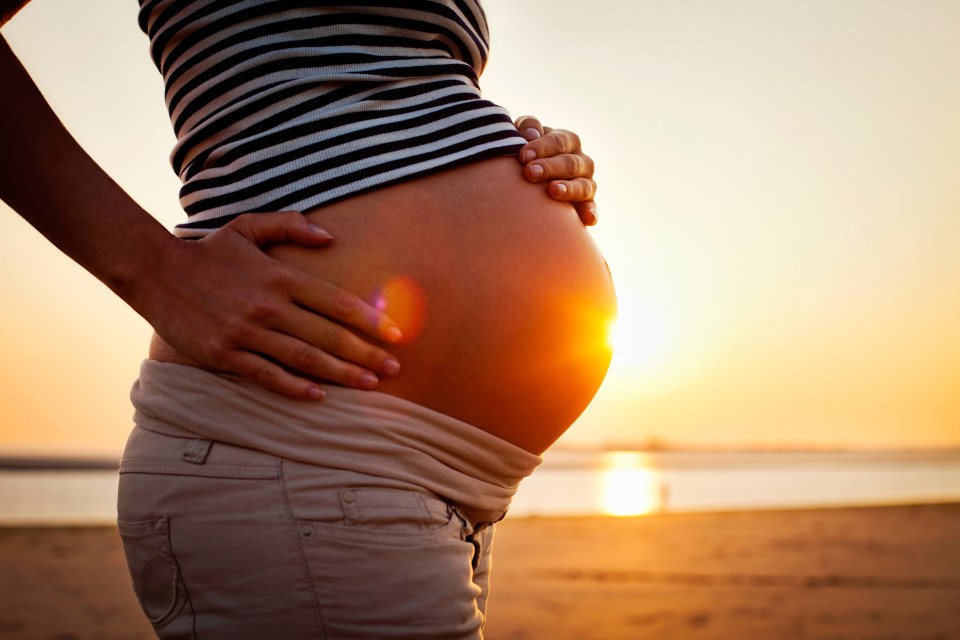 Pregnant woman holding bump on beach at sunset.