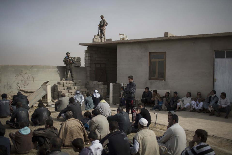 Displaced families sit outside a mosque guarded by Iraqi soldiers