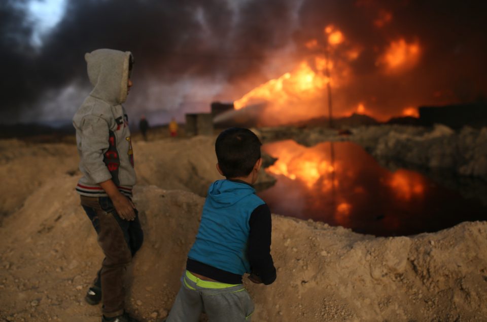  Children watch in aw as oil fires light up the sky near the battleground of Mosul