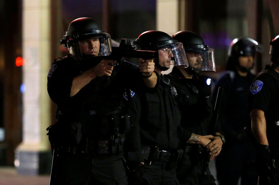  A police officer aims a launcher after demonstrators threw projectiles toward a line of officers