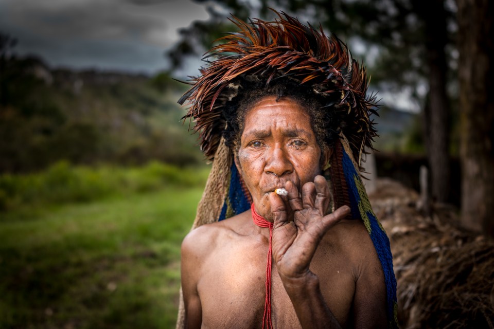 Dani tribeswoman smokes a cigarette and shows her amputated fingers