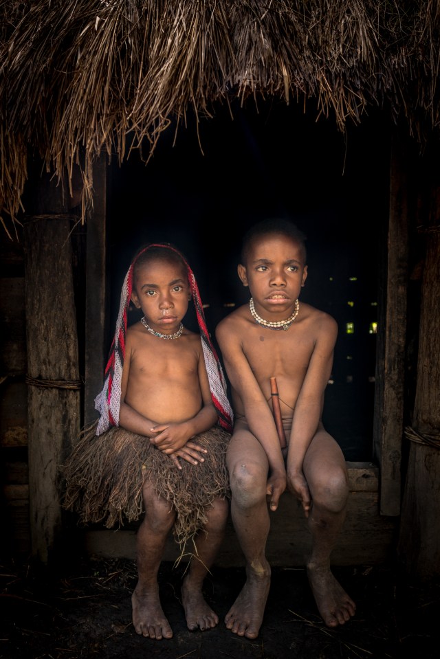 A young boy and girl from Dani tribe sit inside a hut in their village