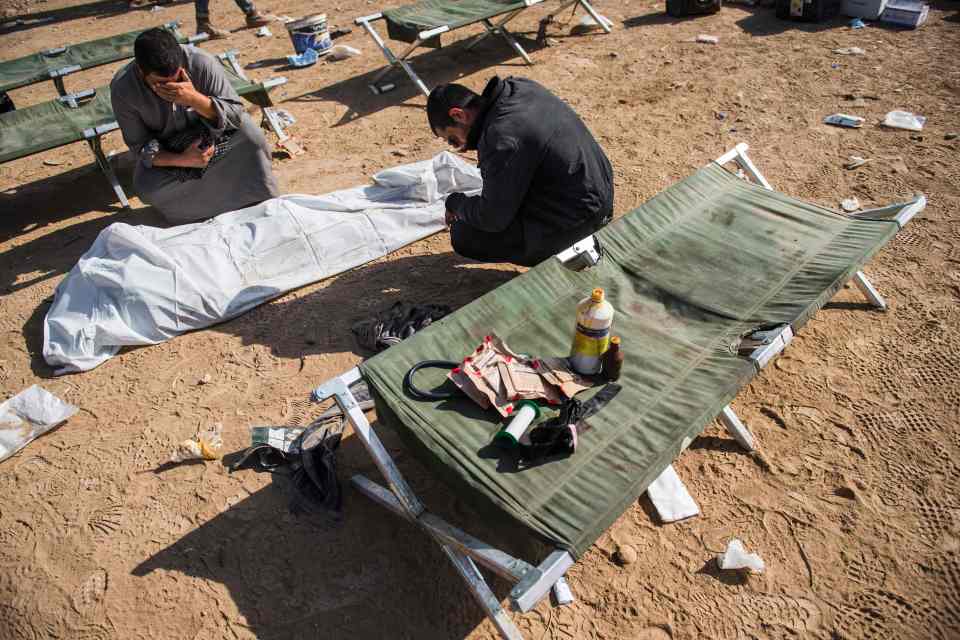  Two men mourn over the body of a relative at an open air field clinic