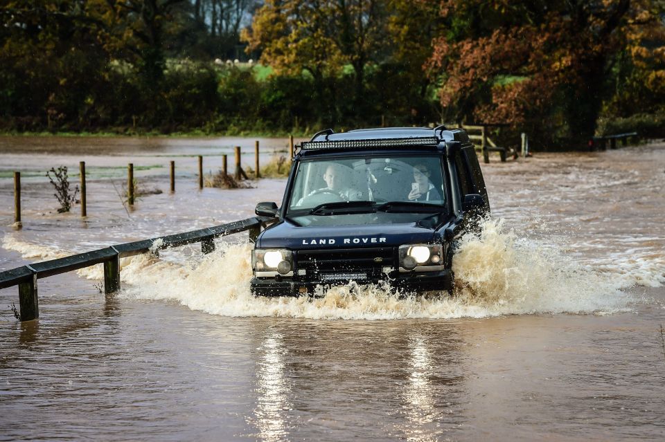 A 4x4 Land Rover ventures through deep flood water on Station Road, Broadclyst, Devon, where rivers have burst their banks