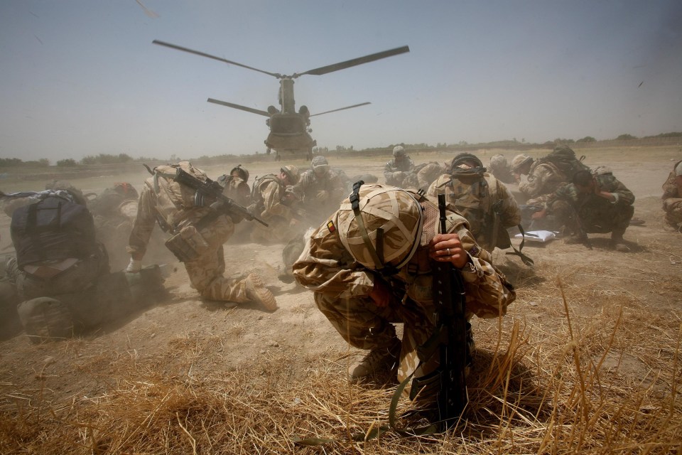 British soldiers of the Royal Anglians take cover from dust as an helicopter takes off from Sangin Base in Sangin, Helmand Province, Afghanistan.