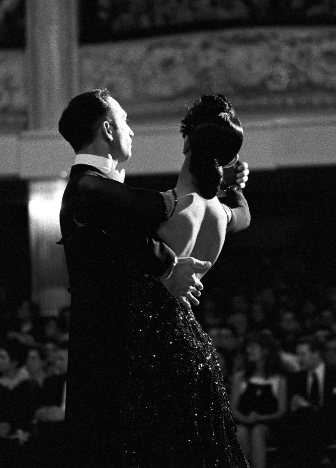  A dancer in a back-revealing sparkly black gown and her partner dazzle on the stage as spectators look on