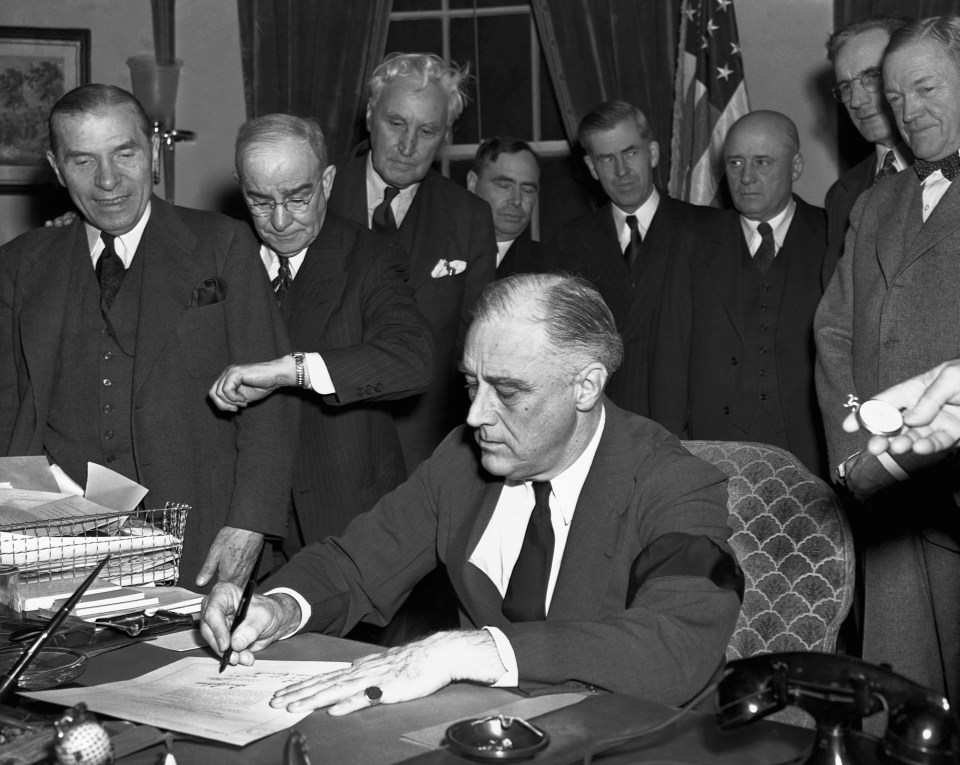 Cabinet members watch with mixed emotions as President Franklin D. Roosevelt, wearing a black armband, signs the United States' declaration of war against Japan