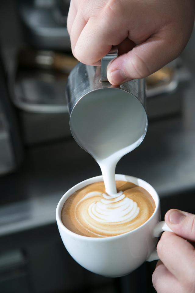 A barista pouring hot milk into a fresh coffee cup to make a latte