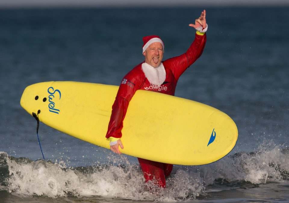 A surfing Santa gestures as he carries his board out of the sea