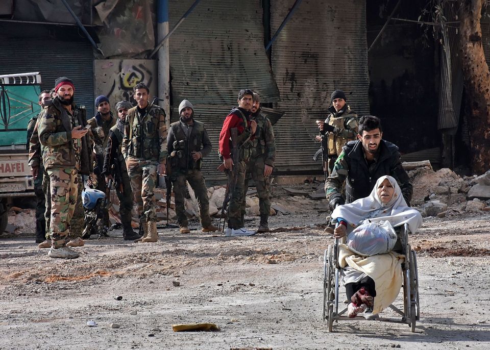  Soldiers watch as an elderly woman is wheeled away from her home by a member of government forces