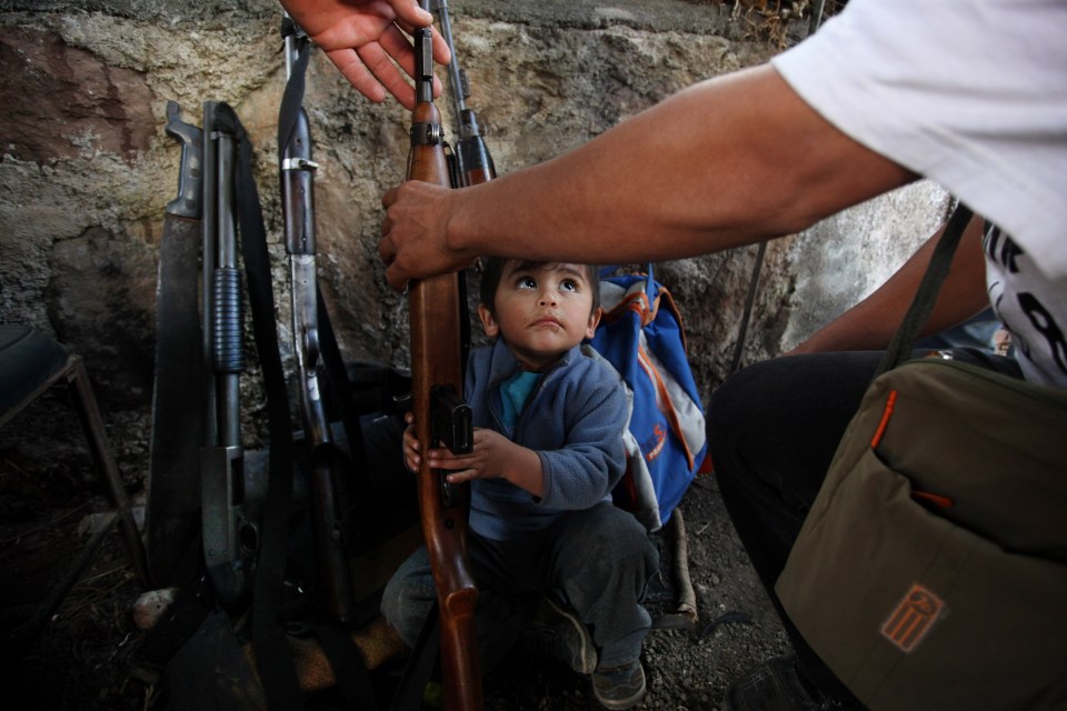  A child helps his father arrange weapons at a checkpoint set up by the Self-Defense Council of Michoacan