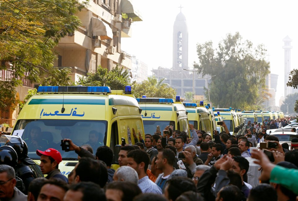  A row of ambulances, mobbed by mourners, drives the coffins from the church after the funeral