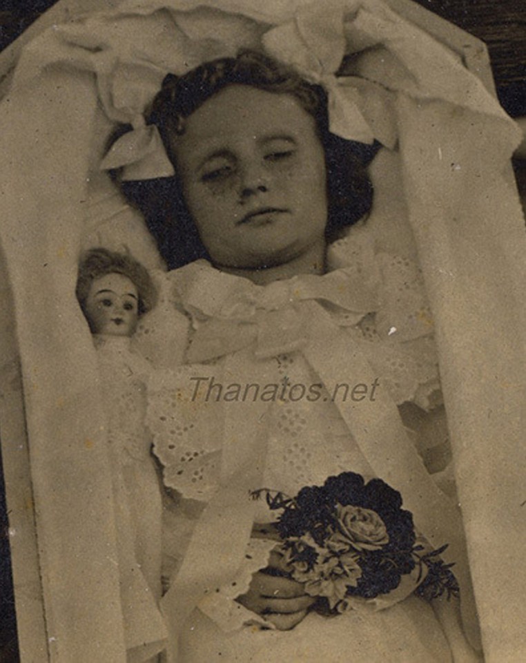  Posed in a lined coffin and clutching a small bunch of flowers, the deceased child is laid to rest with her doll