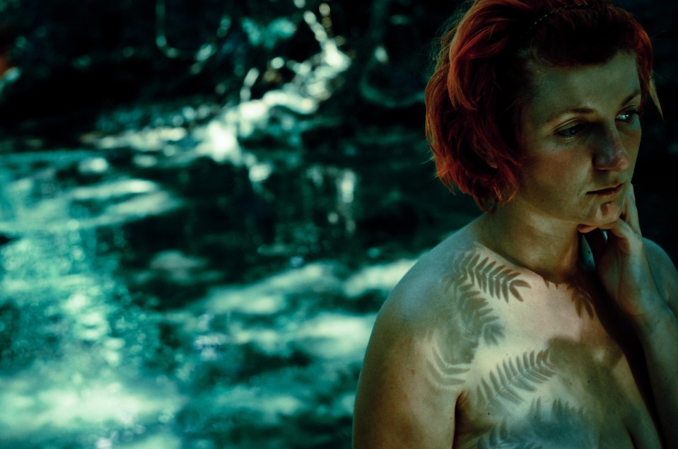 A red-headed woman strips off and shows her tattoos at one event in a tropical forest