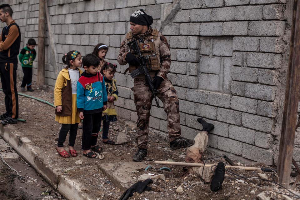  Iraqi children look at the body of a half-buried Islamic State militant while talking to an Iraqi soldier in the al-Barid district in Mosul, Iraq