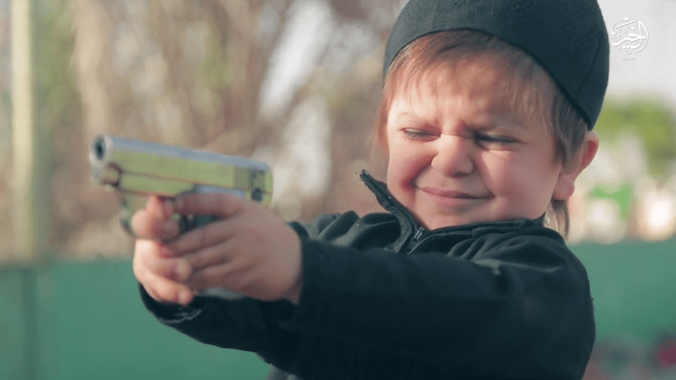  The extremely young boy closes his eyes as he fires a gun at one of the victims