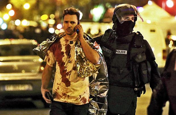 A victim injured in the Paris terror massacre is escorted from the scene by a cop