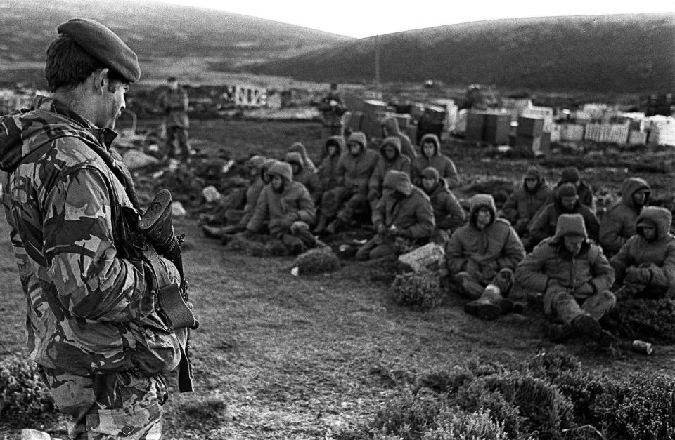  A member of the Royal Marines stands over Argentinian soldiers captured at the Battle of Goose Green