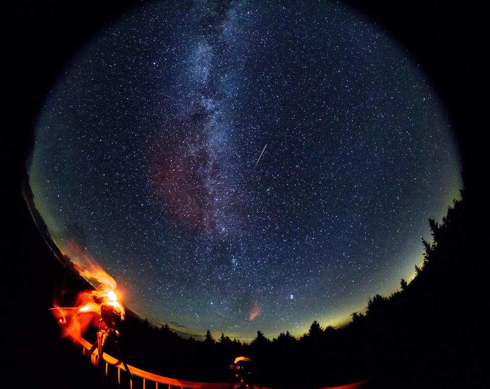  A meteor streaks across the sky during the annual Perseid meteor shower as a photographer wipes moisture from the camera lenses