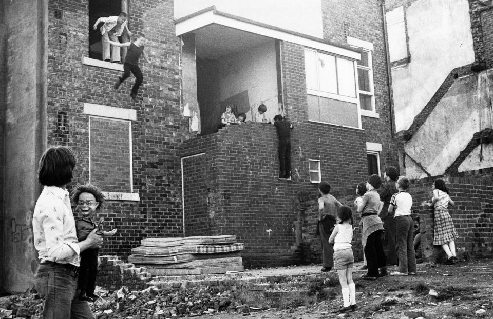  This image shows a boy leaping from an upper window of a derelict house onto a pile of old mattresses