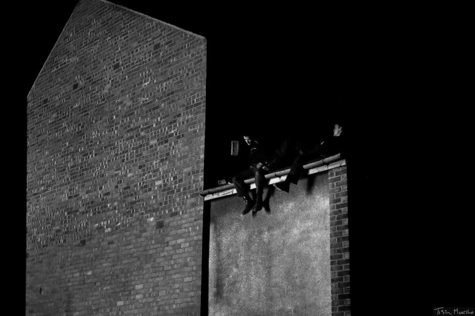  Two men recline on the roof of a building in the dark