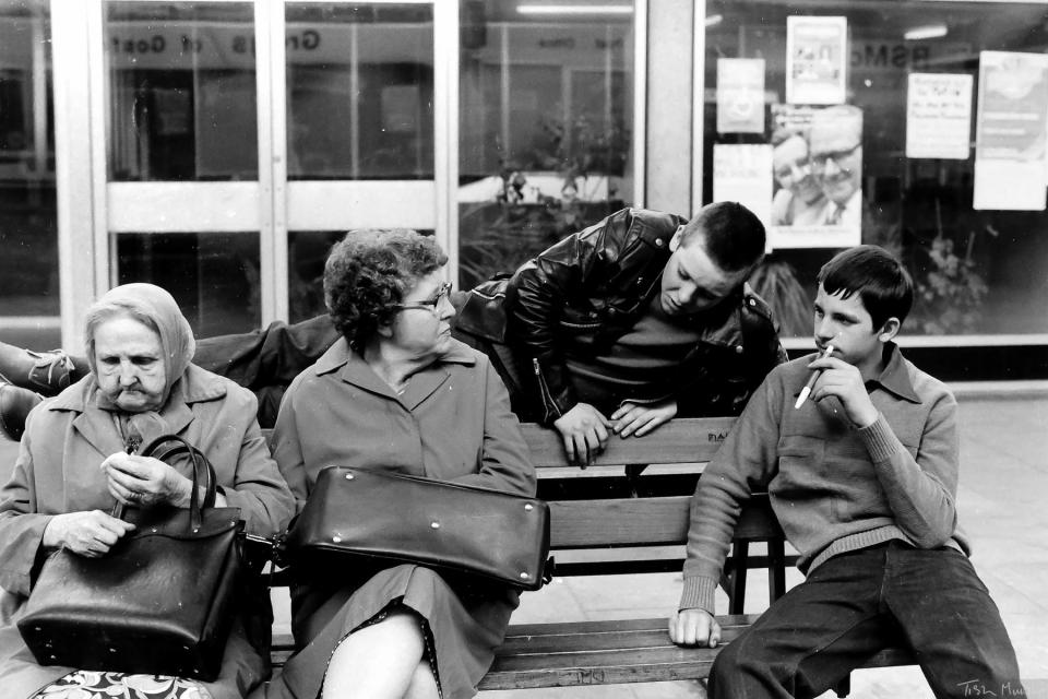  Two youngsters lounge on a bench in the city next to two old women