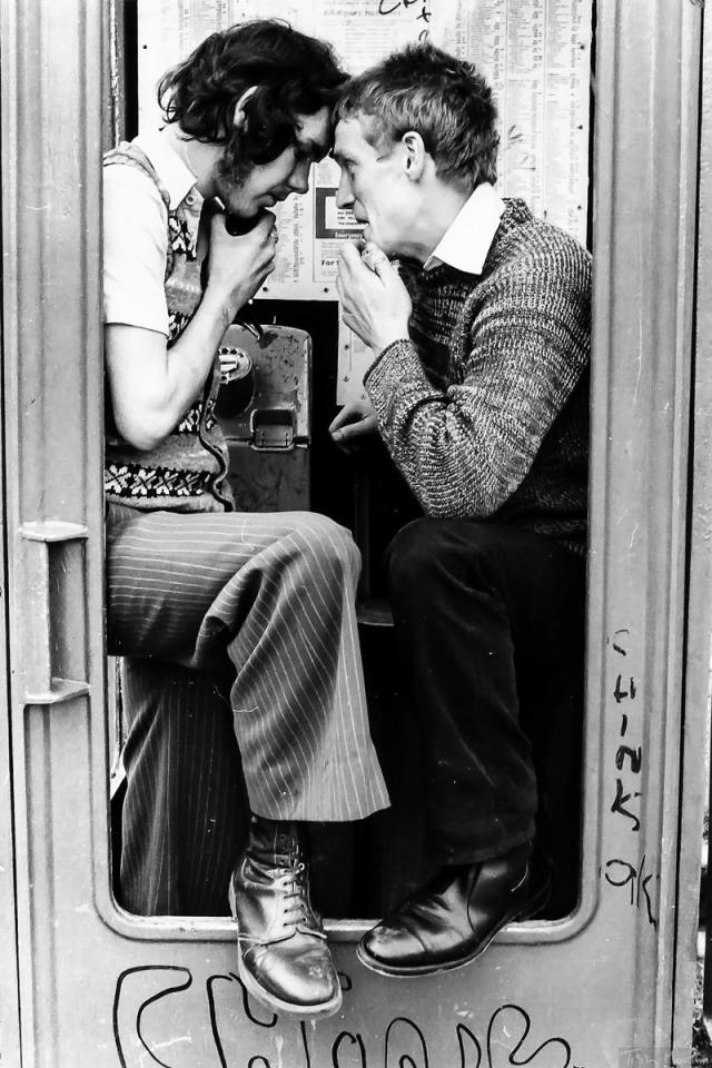  Two men gather round a pay phone covered in graffiti