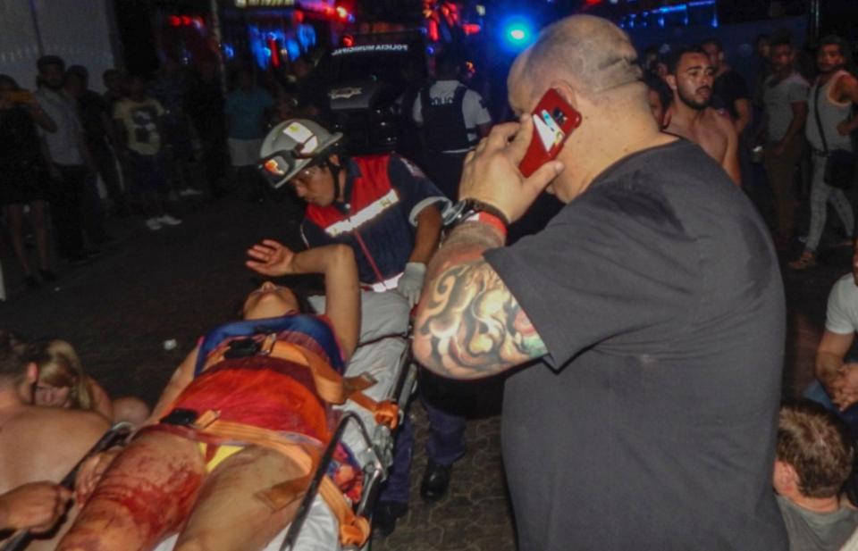  A woman whose leg is covered in blood is carried on a stretcher through a crowd of panicked partygoers