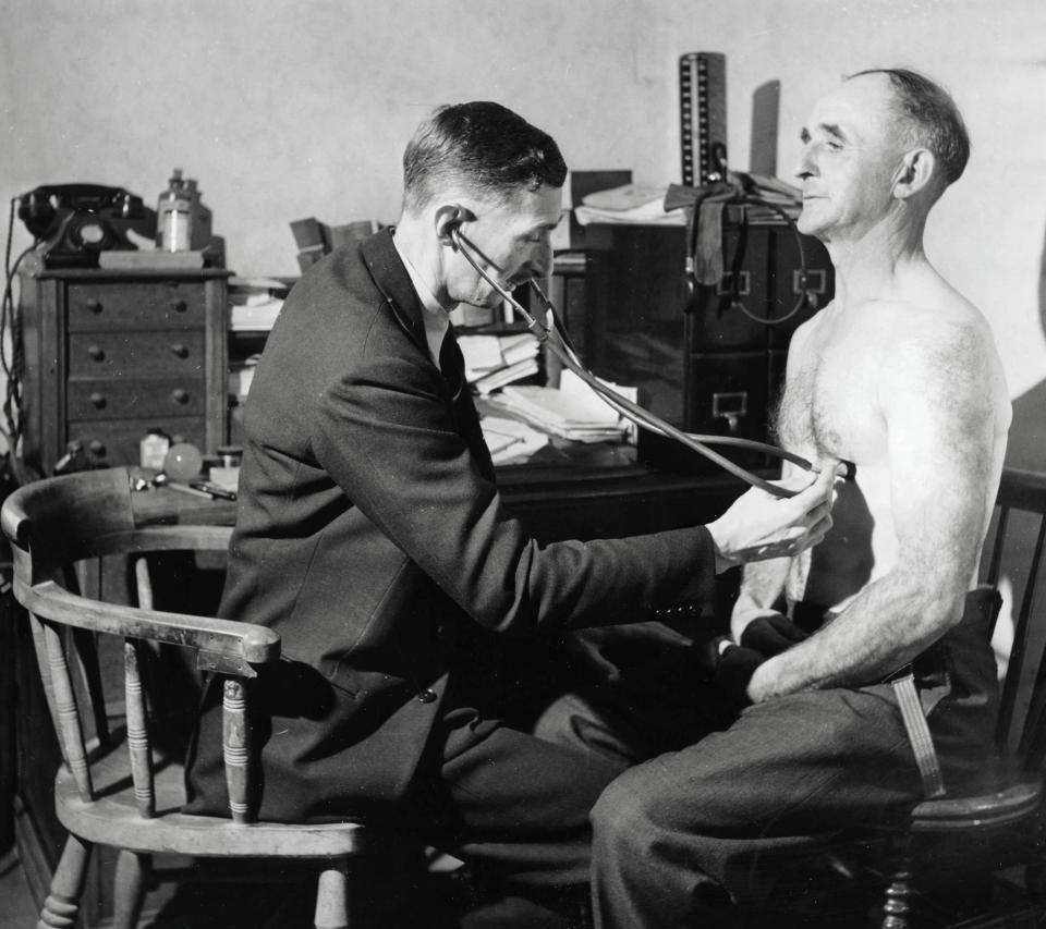  A doctor using a stethoscope to listen to a man's breathing and lungs at an NHS GP clinic