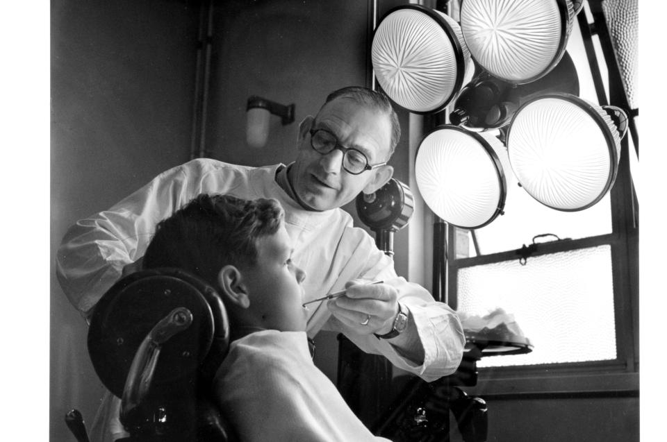 A dentist at a Bristol health centre surgery examines one of his young patient. At the time this service was for schoolchildren and expectant mothers