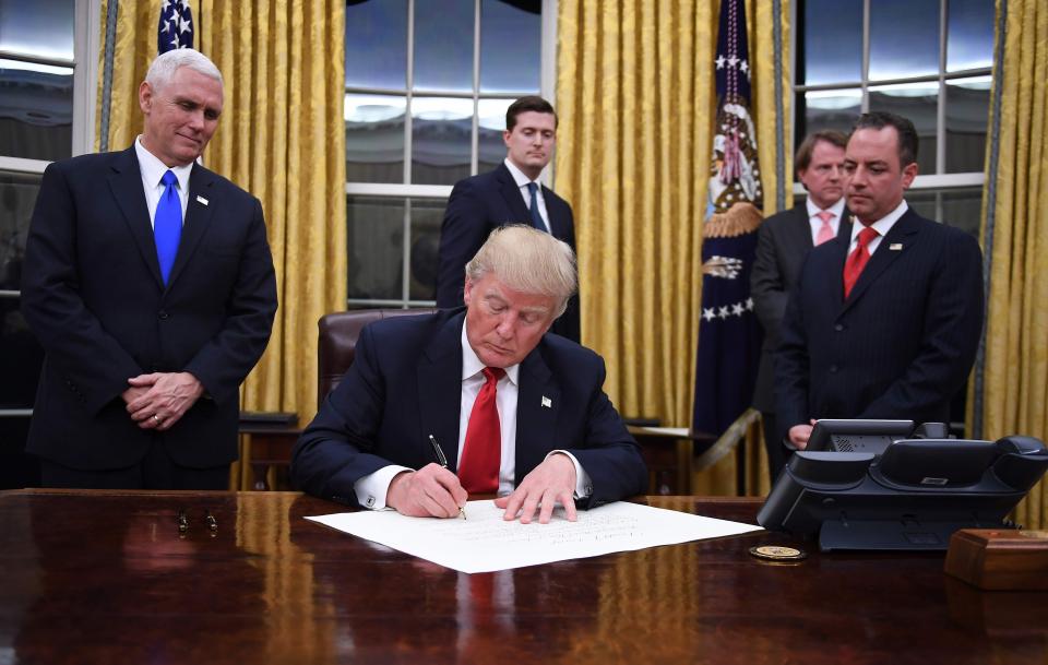  Donald Trump signs an executive order in the Oval Office as Vice President Mike Pence and Chief of Staff Reince Priebus look on