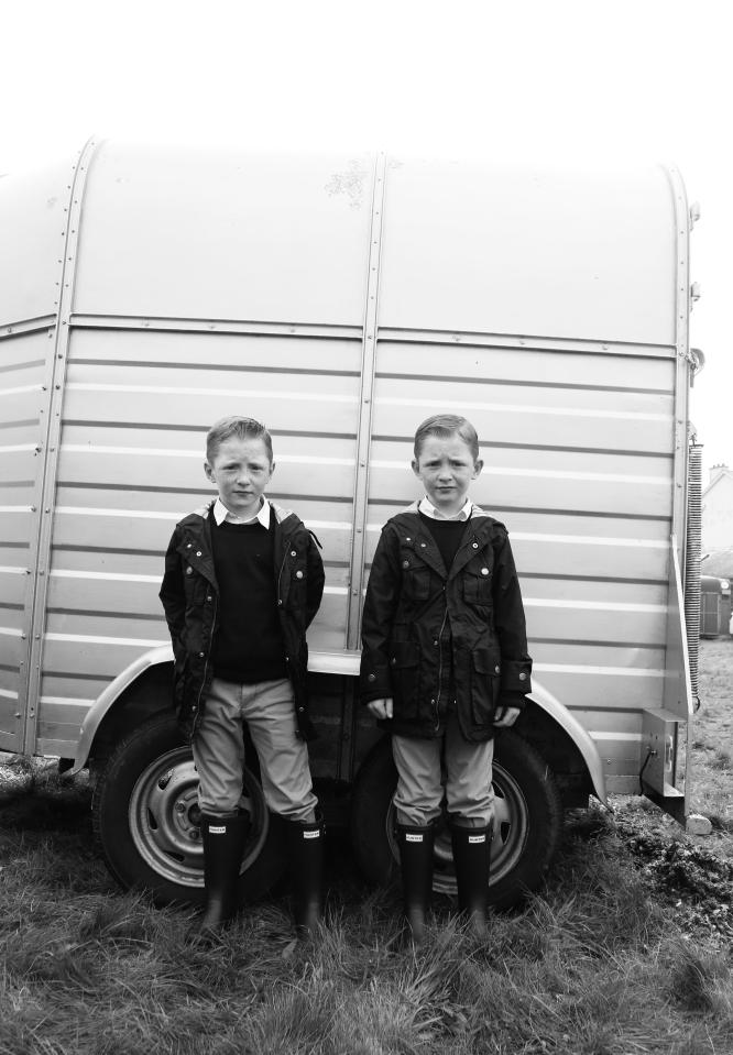  Twin brothers in matching outfits pose by a horse box