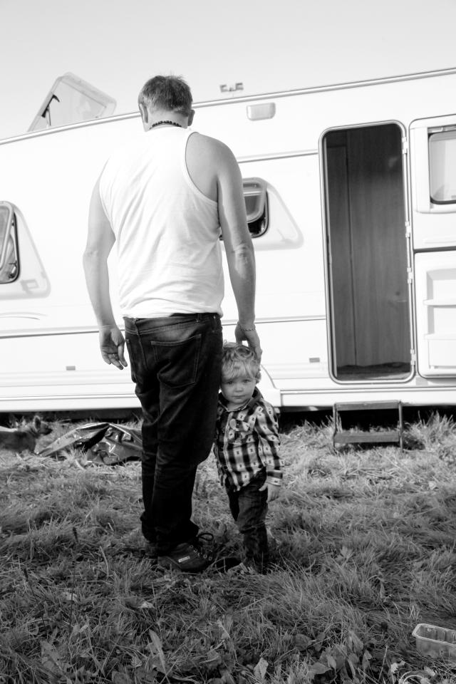  A tot clings on to his dad's leg outside the caravan