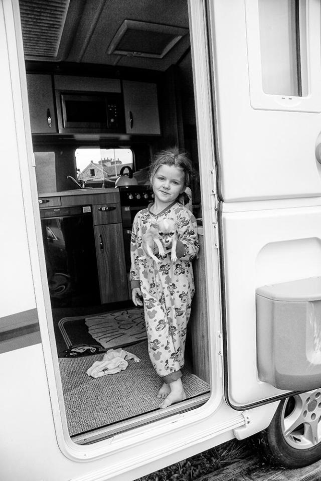  A sleepy little girl holds her dog in the door of her home