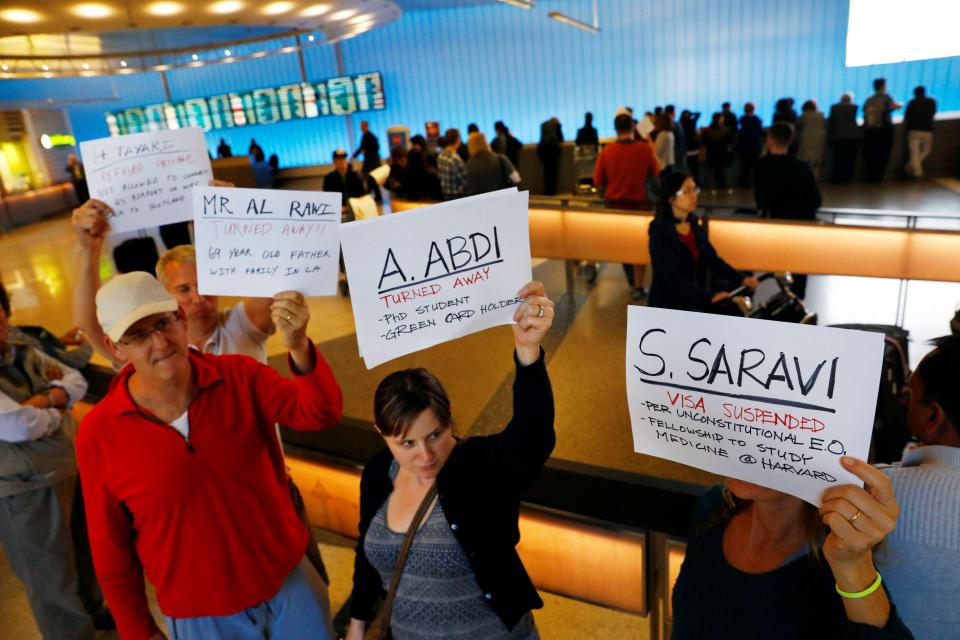 People hold signs with the names of people detained and denied entry