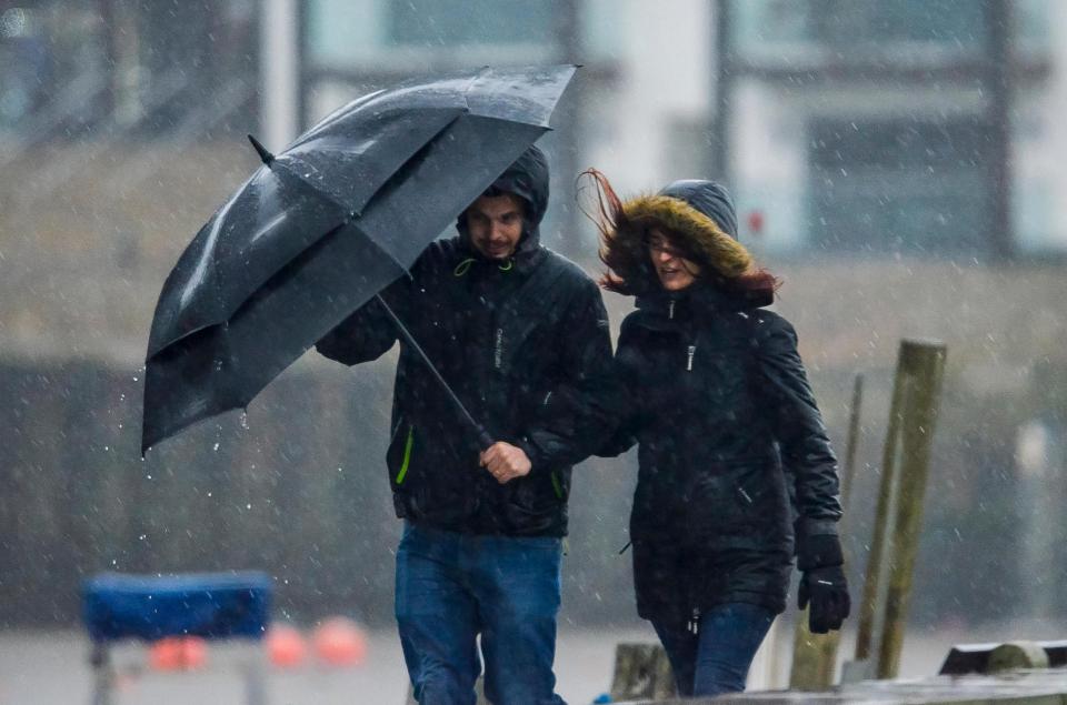  A couple struggling with an umbrella in the strong breeze as heavy rain falls at West Bay in Dorset in January