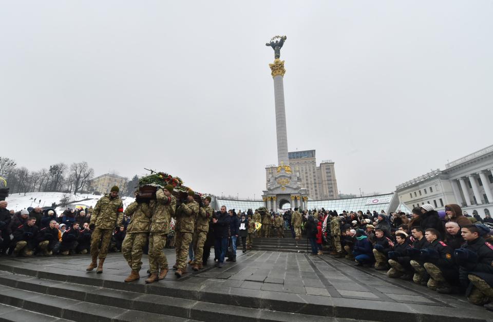  People kneel during a mourning ceremony on Independence Square in Kiev as servicemen carry the coffins with the bodies of seven Ukrainian servicemen