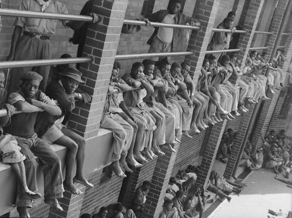  1946: View of barefoot miners as they sit over the edge of a landing that overlooks a courtyard in the Robinson Deep mine compound, Johannesburg, South Africa