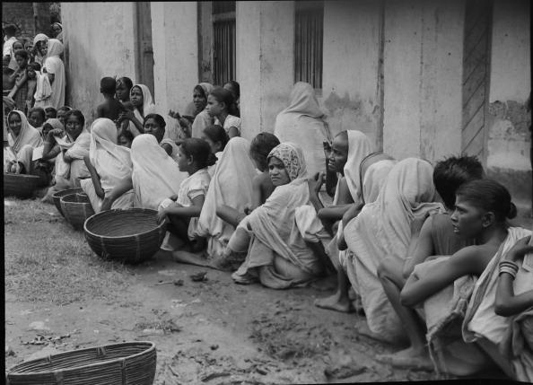  1946: In the aftermath of riots, a line of people sit beside a wall, Calcutta, India